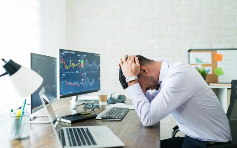 side-view-stressed-young-broker-sitting-with-head-hands-desk-while-working-from-home side-view-stressed-young-broker-sitting-with-head-hands-desk-while-working-from-home